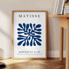 Poster of Matisse-style paper cutout composition in white and green - beside a round wooden side table with books