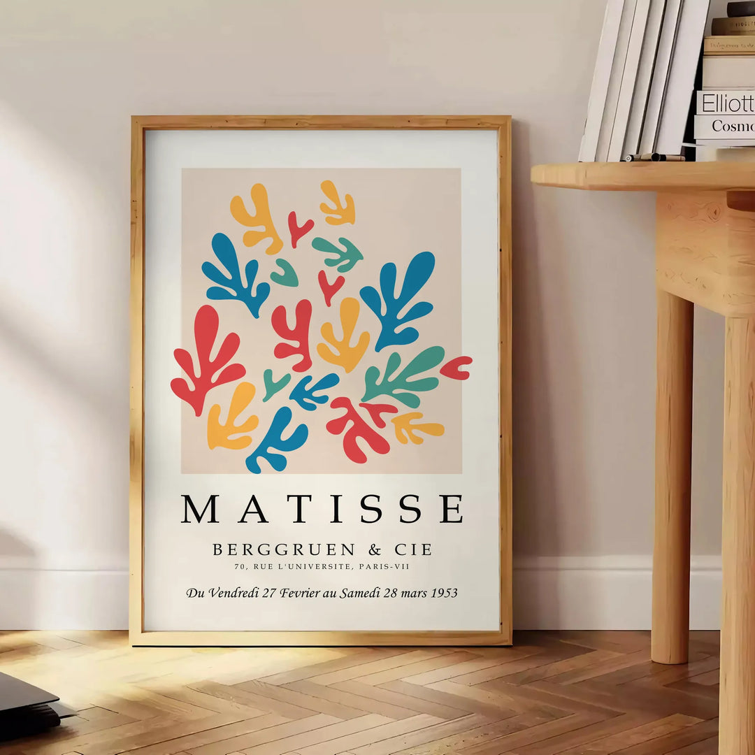 Poster showing colorful abstract paper cutouts in Matisse style artwork - beside a round wooden side table with books