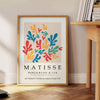 Poster showing colorful abstract paper cutouts in Matisse style artwork - beside a round wooden side table with books