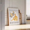 Poster showing Matisse-style papier découpés with bold colorful abstract shapes - leaning on a herringbone floor against a white panelled wall