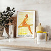 Vintage travel poster of Monte Carlo with warm brown and orange tones - styled on a counter with eucalyptus and a bowl of lemons