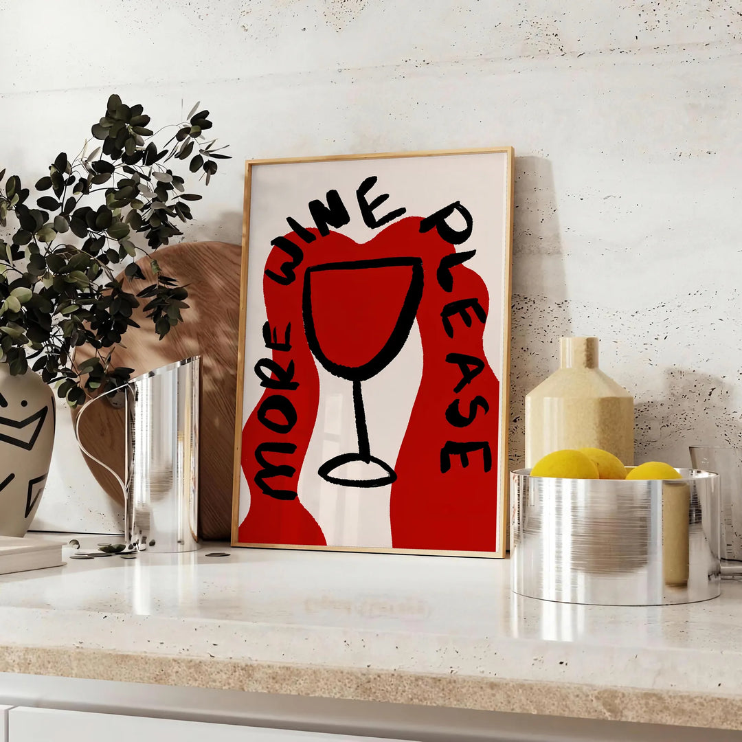 Una stampa da cucina minimalista con la frase 'More Wine Please' in lettere nere su sfondo grigio - su un piano con eucalipto e una ciotola di limoni