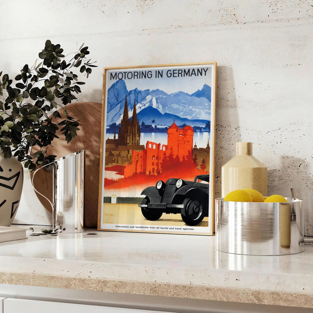A vintage travel poster featuring a classic car on a road in Germany, with orange and blue tones. - styled on a counter with eucalyptus and a bowl of lemons