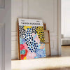 Colorful abstract nature scene by Yayoi Kusama with polka dots - leaning on a herringbone floor against a white panelled wall