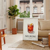 Illustration of a Negroni cocktail in a sleek glass, with orange and black colors - in a Parisian living room with a sofa and a fig plant