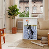 A travel poster featuring New York's skyline in black and orange hues - in a Parisian living room with a sofa and a fig plant