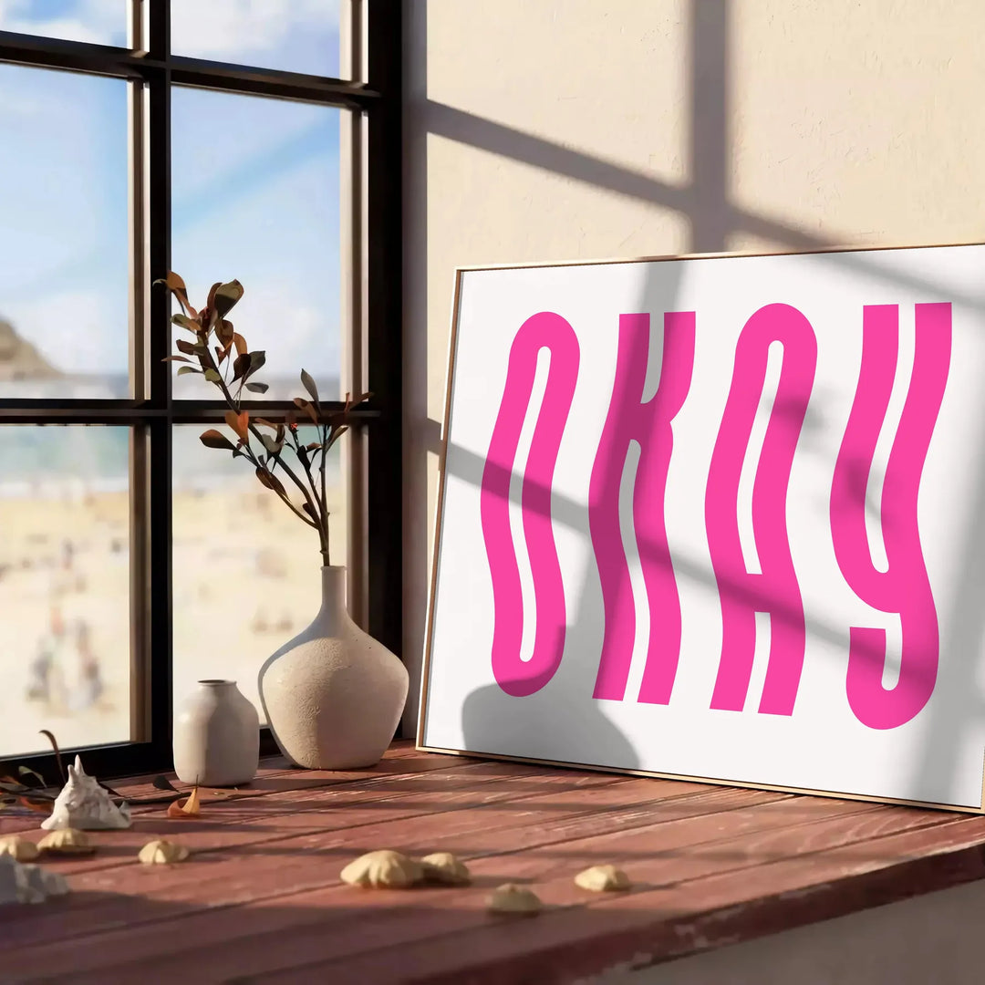 Motivational poster with the phrase 'Okay' in pink and white colors - leaning on a herringbone floor against a white panelled wall