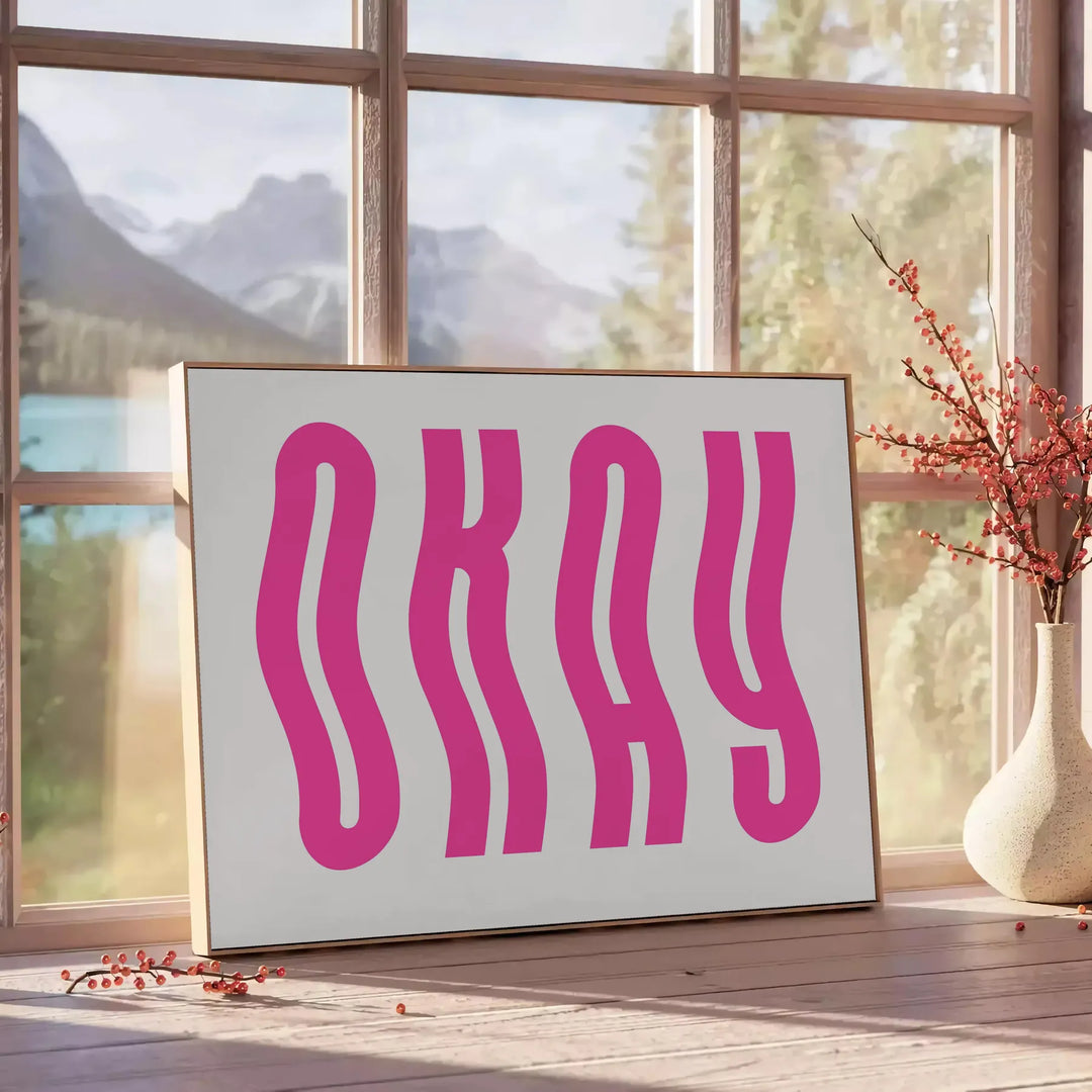 Motivational poster with the phrase 'Okay' in pink and white colors - beside a round wooden side table with books