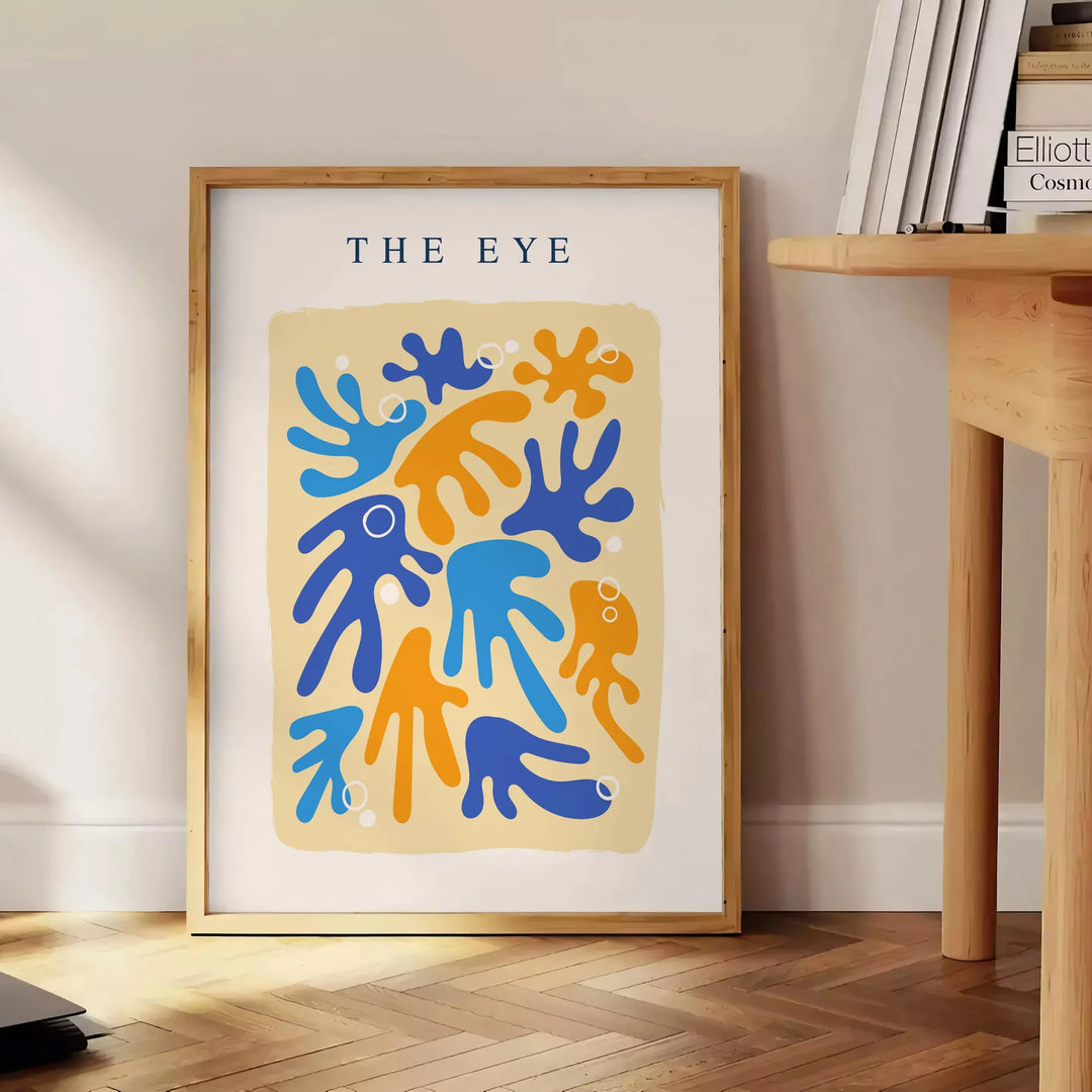 Poster de arte em papel recortado espaço em tons cinza e laranja - ao lado de uma mesa de apoio redonda em madeira com livros