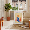 Poster showing layered papier découpé space artwork in orange and blue - in a Parisian living room with a sofa and a fig plant