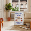 blue and white poster featuring 'Pasta Lover Club' text with pasta illustrations - in a Parisian living room with a sofa and a fig plant