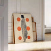 Stylish gray poster with vibrant orange abstract shapes - leaning on a herringbone floor against a white panelled wall