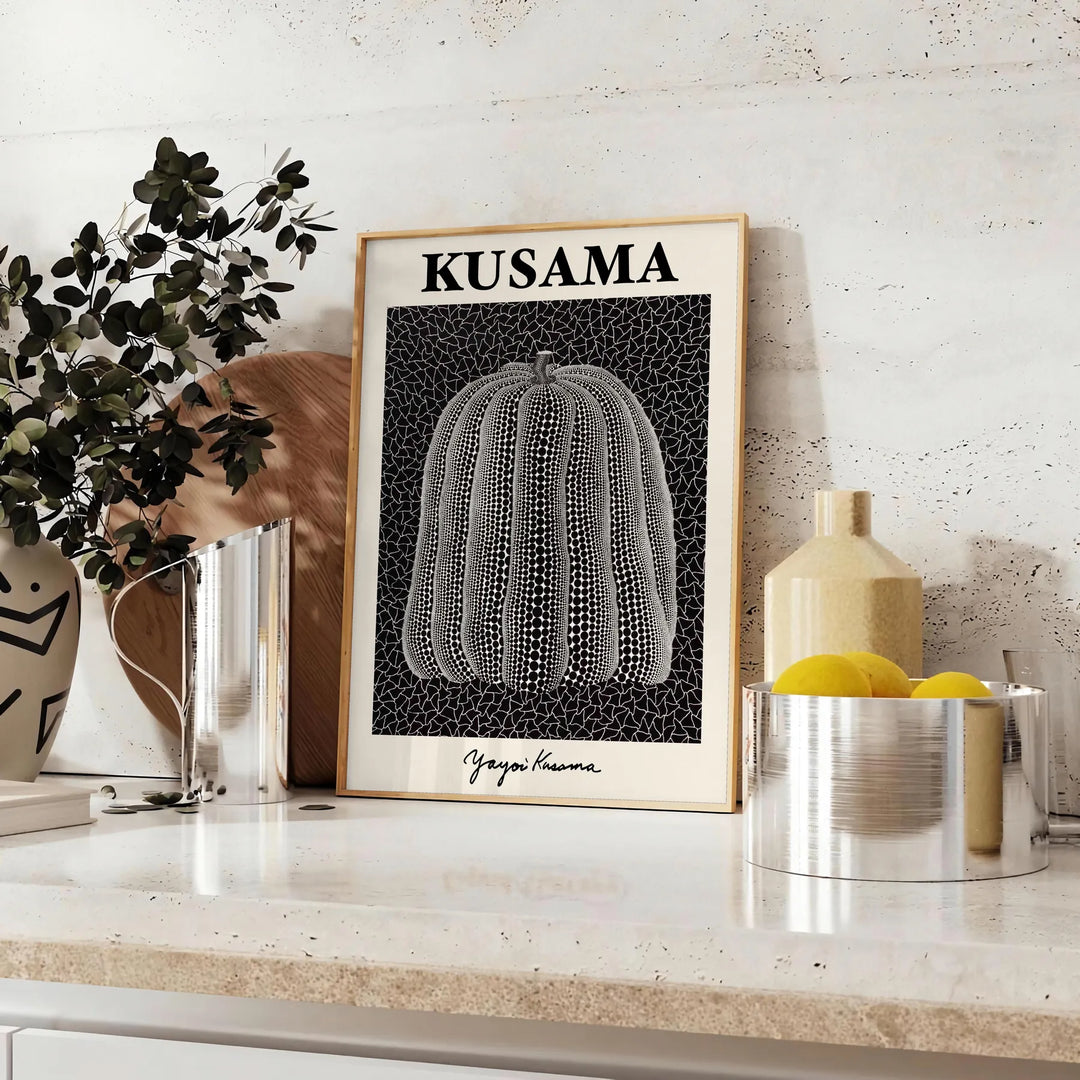 A bright orange pumpkin covered in black polka dots by Yayoi Kusama - styled on a counter with eucalyptus and a bowl of lemons