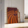 Yayoi Kusama pumpkin artwork with rich brown and green hues - leaning on a herringbone floor against a white panelled wall
