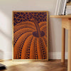 Yayoi Kusama pumpkin artwork with rich brown and green hues - beside a round wooden side table with books