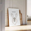 A rabbit in a serene gray and black color palette - leaning on a herringbone floor against a white panelled wall