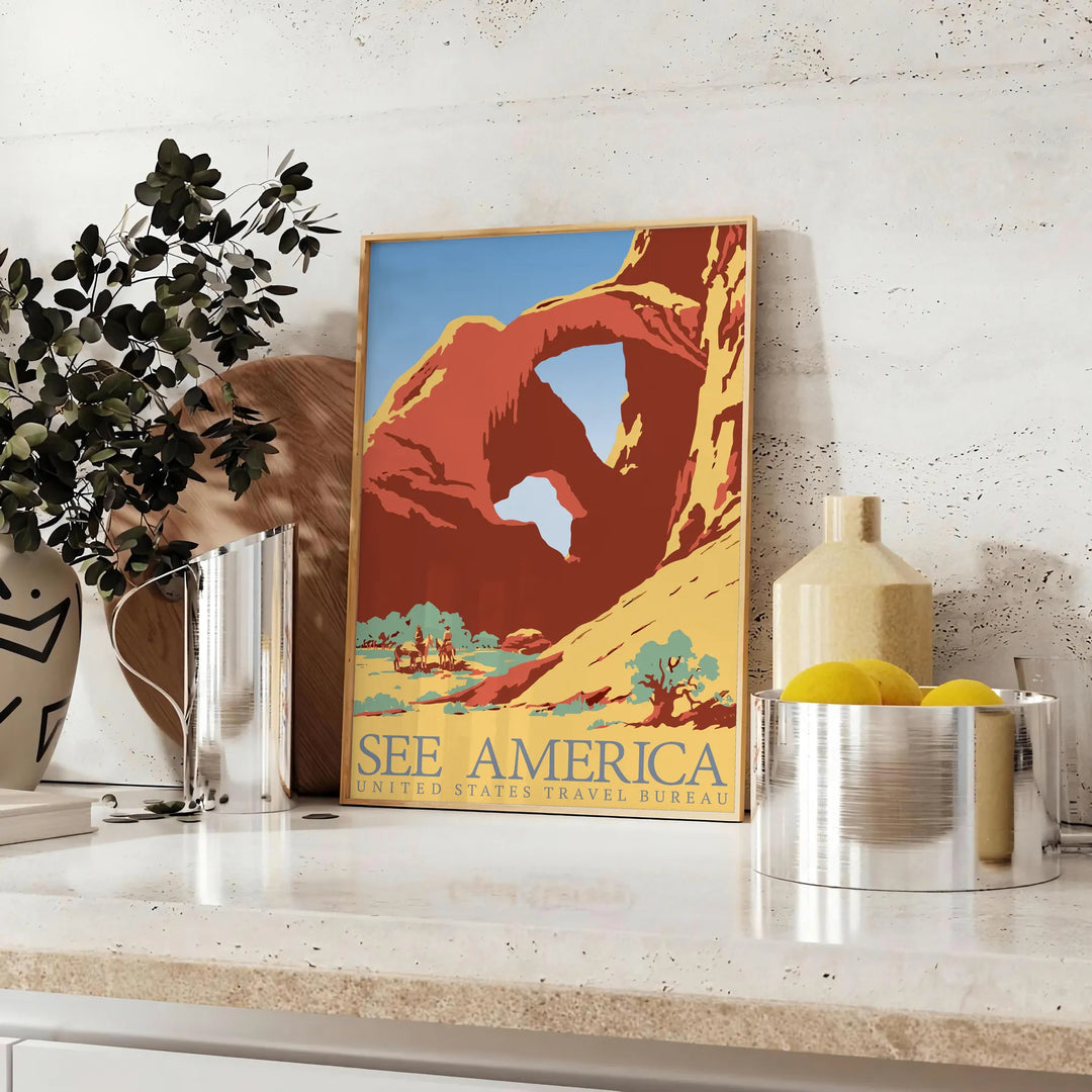 A retro travel poster featuring a yellow and blue landscape with mountains and a road - styled on a counter with eucalyptus and a bowl of lemons