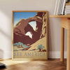 Travel poster featuring a serene landscape of America in gray and green tones - beside a round wooden side table with books