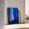 A vintage-style travel poster featuring iconic American landscapes in blue and black tones - leaning on a herringbone floor against a white panelled wall