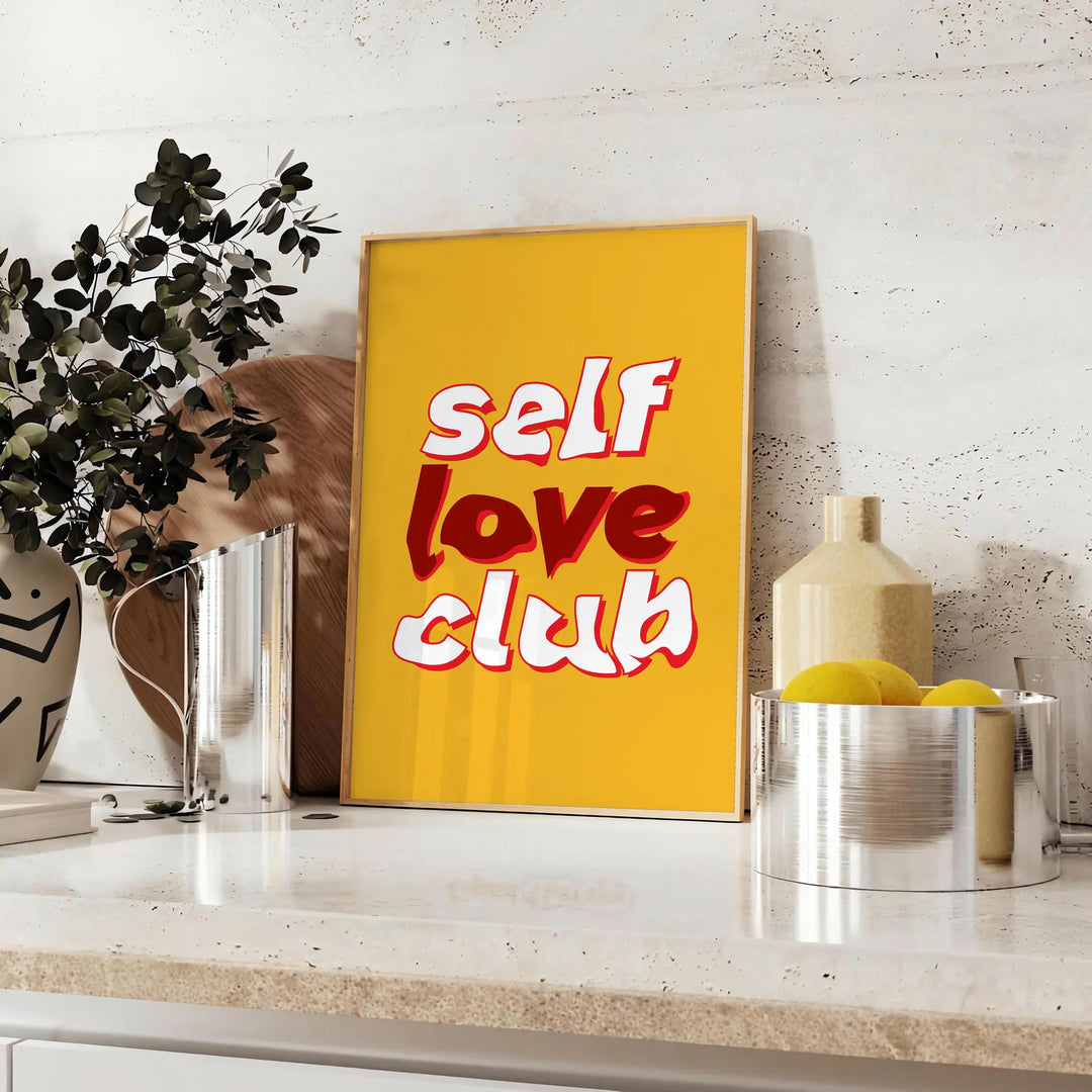 Abstract design featuring the phrase 'Self Love Club' in bold typography with warm orange and red tones - styled on a counter with eucalyptus and a bowl of lemons