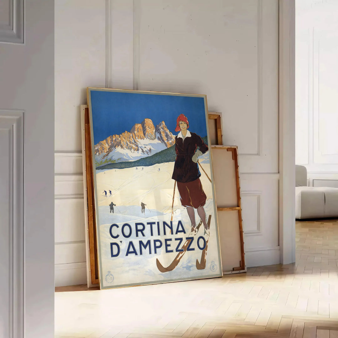 A vintage-style ski travel poster featuring snowy mountains and a bright blue sky - leaning on a herringbone floor against a white panelled wall