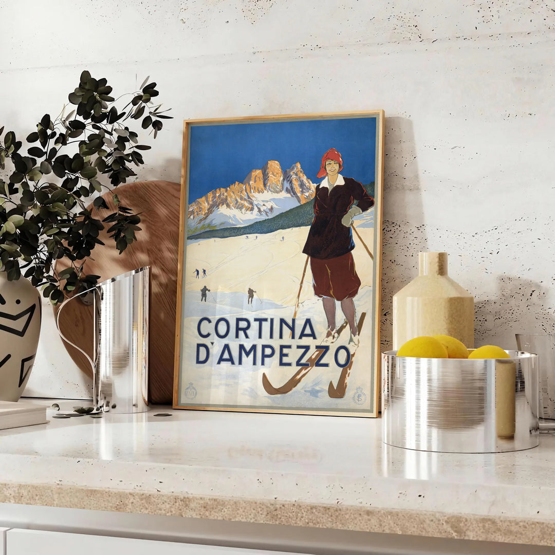 A vintage-style ski travel poster featuring snowy mountains and a bright blue sky - styled on a counter with eucalyptus and a bowl of lemons