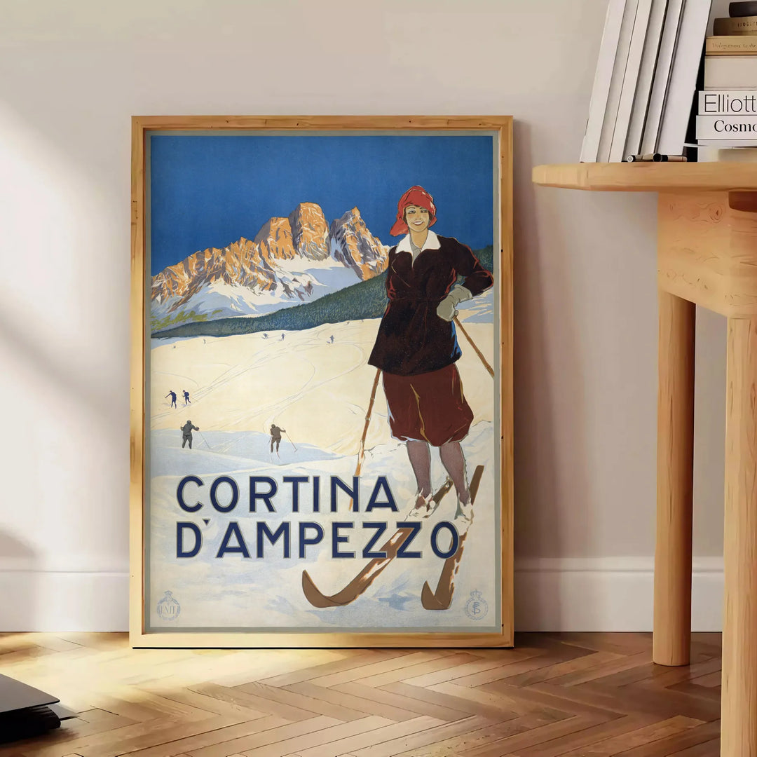 A vintage-style ski travel poster featuring snowy mountains and a bright blue sky - beside a round wooden side table with books