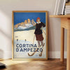 A vintage-style ski travel poster featuring snowy mountains and a bright blue sky - beside a round wooden side table with books