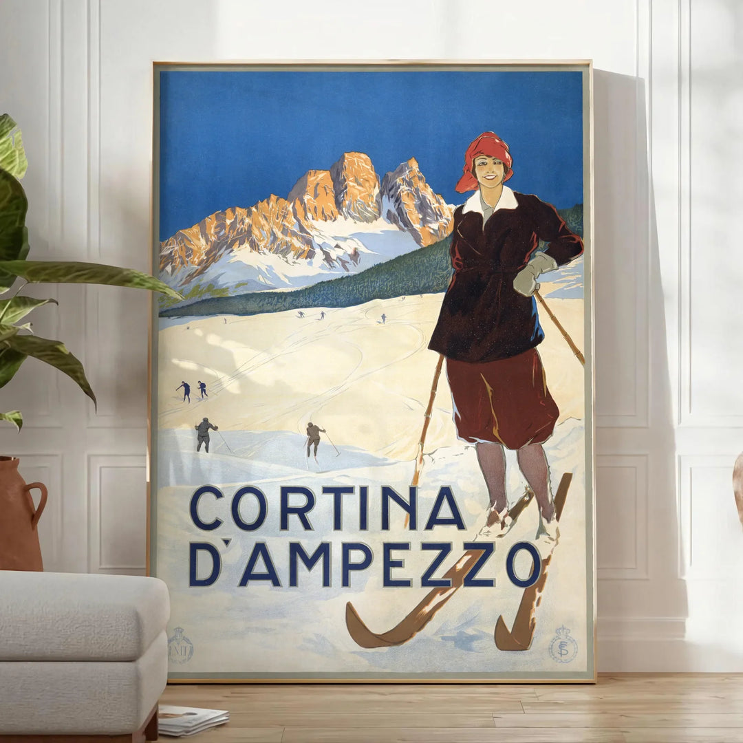 A vintage-style ski travel poster featuring snowy mountains and a bright blue sky - in a bright minimalist room with a plant and an armchair
