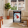 A minimalist ski travel poster featuring a snowy mountain landscape in gray and black tones - in a Parisian living room with a sofa and a fig plant