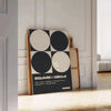 Abstract composition of squares and circles in black and brown tones - leaning on a herringbone floor against a white panelled wall