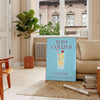Illustration of a Tom Collins cocktail in a glass with lemon and cherry, yellow and blue colors - in a Parisian living room with a sofa and a fig plant