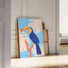 A colorful toucan perched on a branch with bright orange and blue feathers - leaning on a herringbone floor against a white panelled wall