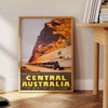 Illustration of a train traveling through lush Australian landscapes in green and blue tones - beside a round wooden side table with books