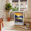 A vintage-style train travel poster featuring a gray and blue color palette - in a Parisian living room with a sofa and a fig plant