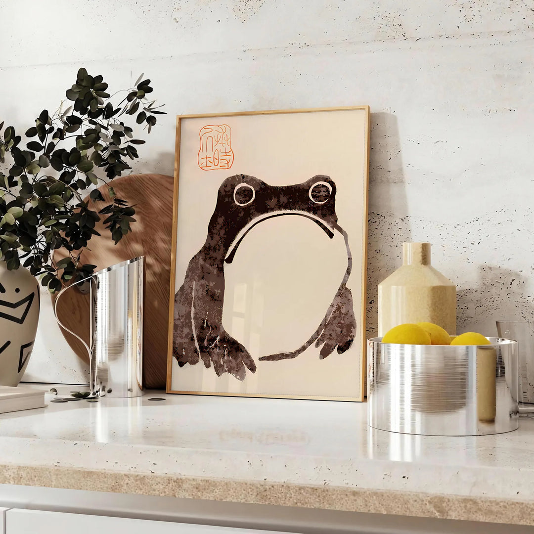A frog with an unimpressed expression against a black and orange background - styled on a counter with eucalyptus and a bowl of lemons