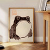 A frog with an unimpressed expression against a black and orange background - beside a round wooden side table with books