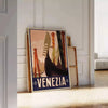 A vintage-style poster featuring iconic Venice canals and gondolas in green and black tones - leaning on a herringbone floor against a white panelled wall