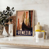 A vintage-style poster featuring iconic Venice canals and gondolas in green and black tones - styled on a counter with eucalyptus and a bowl of lemons