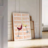 A playful kitchen poster featuring the phrase 'Wine Not' in bold letters, with yellow and purple colors. - leaning on a herringbone floor against a white panelled wall