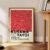 Red dots on a white background with black accents by Yayoi Kusama - beside a round wooden side table with books