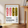 Abstrakte Punktmuster in Orange und Schwarz von Yayoi Kusama - neben einem runden Beistelltisch aus Holz mit Büchern