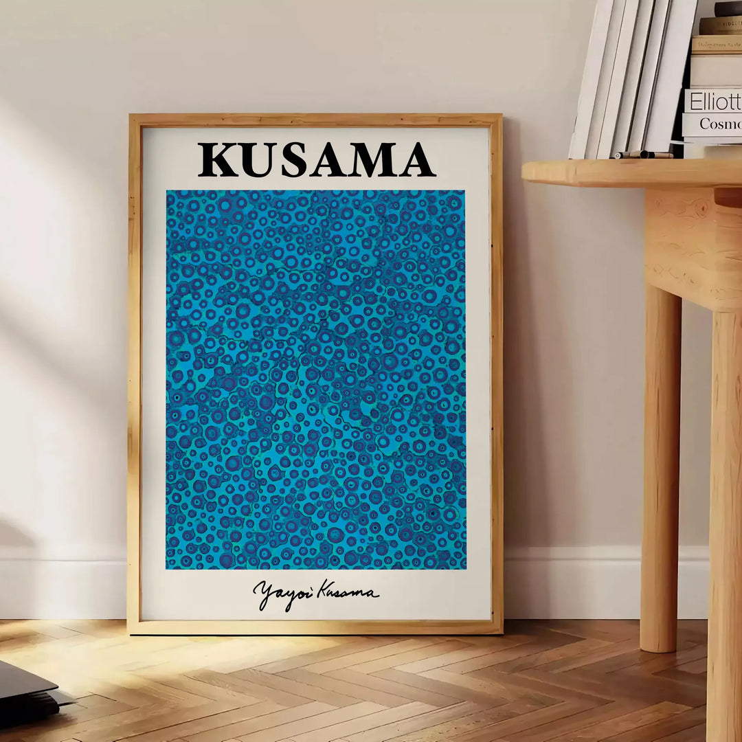 Abstract polka dot patterns in blue and black by Yayoi Kusama - beside a round wooden side table with books
