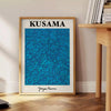 Abstract polka dot patterns in blue and black by Yayoi Kusama - beside a round wooden side table with books