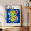 Colorful polka dots in various sizes on a deep blue background by Yayoi Kusama - beside a round wooden side table with books