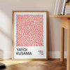 Motivi astratti di pois in arancione e nero di Yayoi Kusama - accanto a un tavolino rotondo in legno con libri