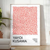 Motivi astratti di pois in arancione e nero di Yayoi Kusama - in una stanza luminosa e minimalista con pianta e poltrona