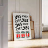 Bold typography featuring 'Yes Chef' in black and red colors - leaning on a herringbone floor against a white panelled wall