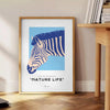 A stylized zebra in shades of blue and gray against a textured background - beside a round wooden side table with books