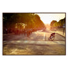 Dynamic cycling scene with cyclists racing through a green landscape under an orange sky - in a walnut frame